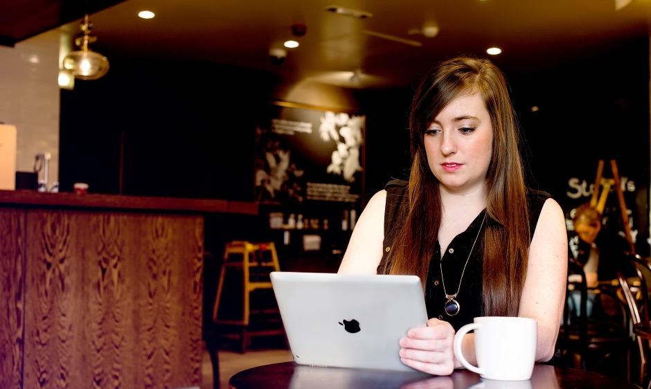 An image of a young woman using an iPad in a coffee shop