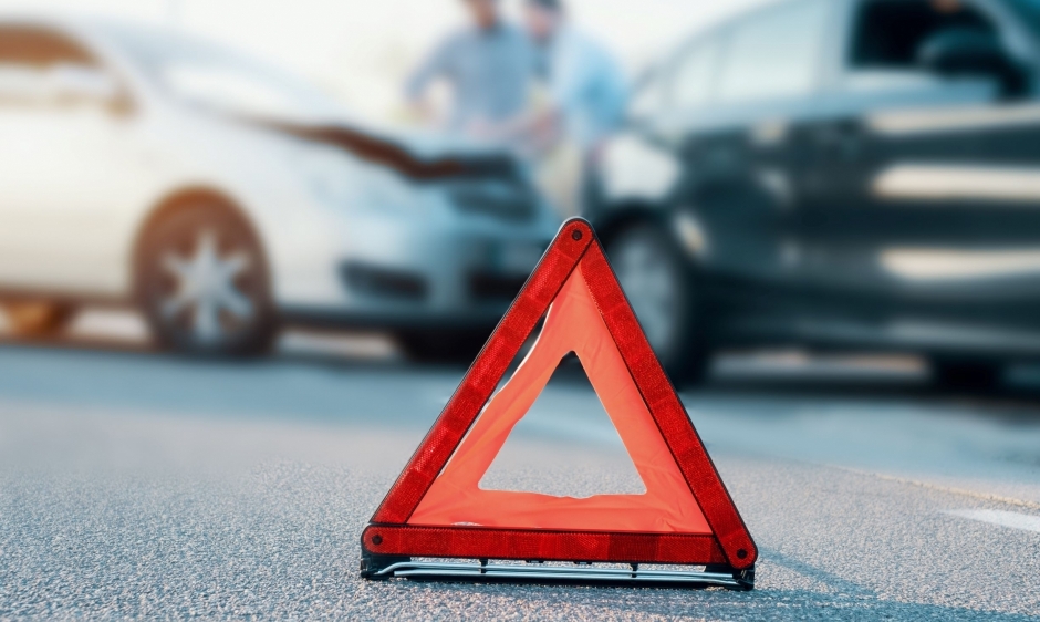 A close up image of a warning triangle with an accident scene blurred in the backgroun