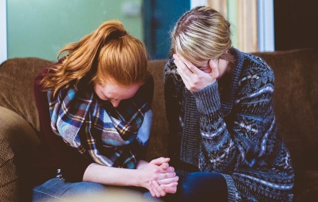 An image of two women sitting side by side on a sofa and looking upset