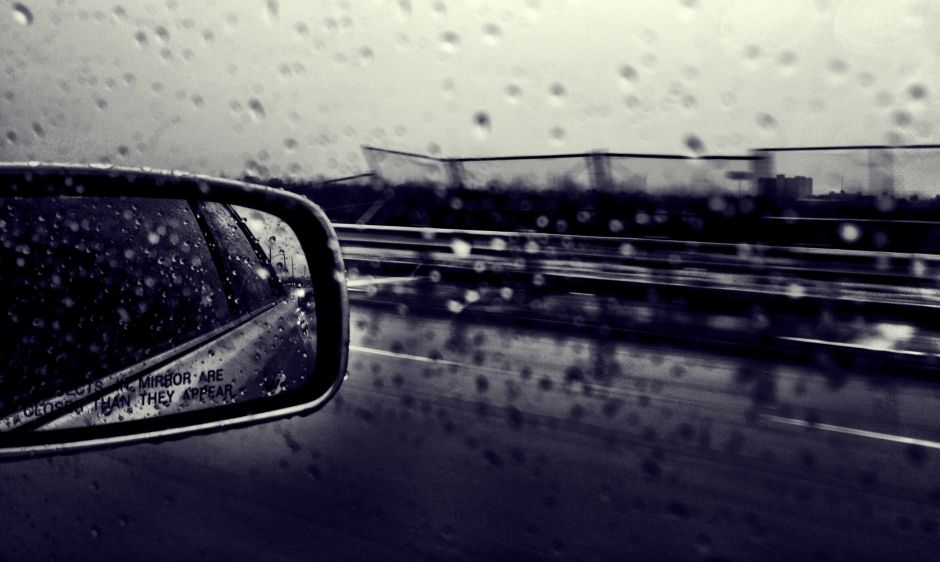 A moody image showing a wing mirror and reflection out of a car window on a rainy day